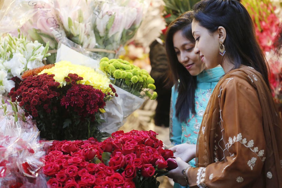 Two women shopping for flowers at a florist in Camden Market. They are examining a vibrant bouquet of red roses with lush, tightly packed petals. Surrounding them are various floral arrangements, incl